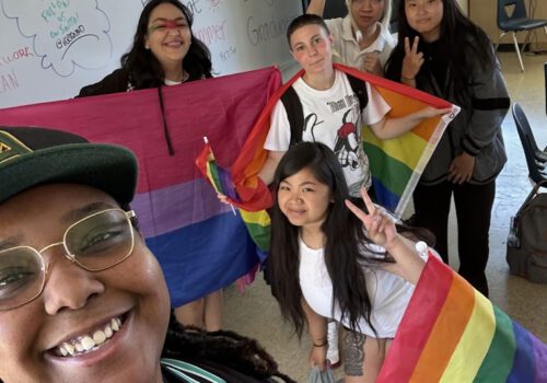 A person taking a selfie style photo of a group/ of kids holding pride flags