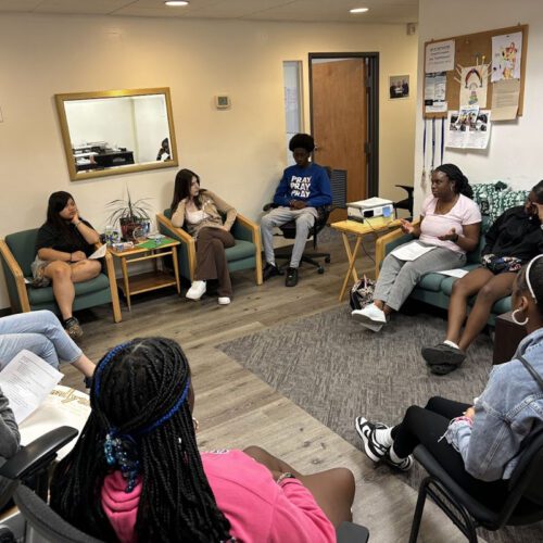 a group of young men and women sitting a circle talking together about mental health